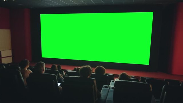 Viewers people are enjoying interesting movie on big green screen copyspace in dark cinema looking with attention. Template, entertainment and films concept.