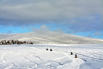 people driving snowmobiles on a snowy field