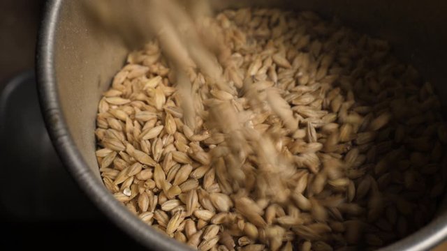 Slow motion shot of barley malt being poured into a mill during the brewing beer process