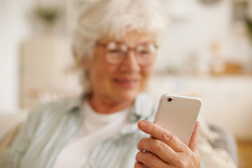 Stylish mature woman with gray hair relaxing in living room, sitting on couch holding cell phone,...