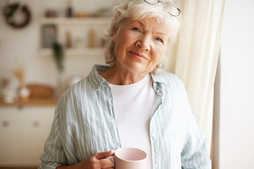 Portrait of charming relaxed female on retirement having morning coffee indoors, standing in...
