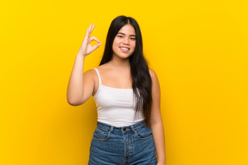 Young teenager Asian girl over isolated yellow background showing ok sign with fingers