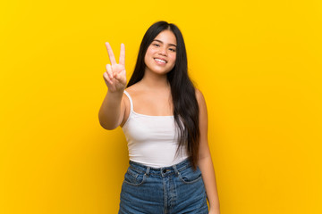 Young teenager Asian girl over isolated yellow background smiling and showing victory sign