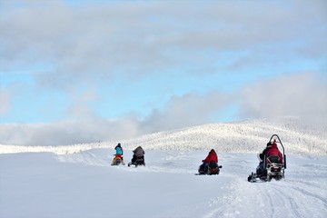 people driving snowmobiles on a snowy field