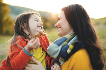 A portrait of young mother with a small daughter in autumn nature at sunset.