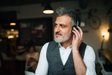 Mature man with headphones at the table in a cafe, using laptop.