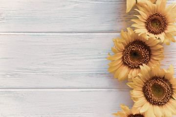 Greeting card design with sunflowers on light wooden background. Frame for text with flowers of sunflower. Photo sunflowers with the place for copywriting. View from above