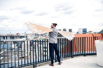 A young businessman with wings standing on a terrace, flying metaphor concept.