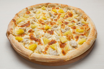 Hawaiian pizza with chicken, pineapple and cheese, on a white wooden table, close-up