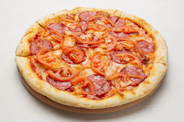 italian pizza with salami sausage, tomatoes and cheese, on a white wooden table