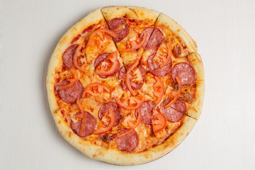 italian pizza with salami sausage, tomato and cheese, on a white wooden table