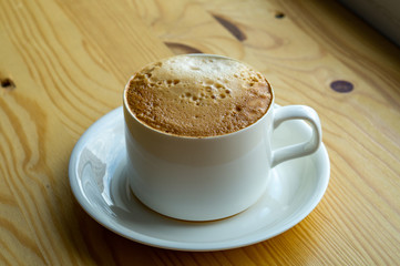 cup of coffee in a white cup stands on a wooden table