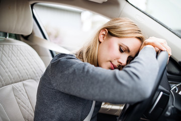 Fototapeta na wymiar Tired young woman driver sitting in car, head resting on steering wheel.