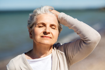 people and leisure concept - portrait of happy senior woman enjoying sun on beach