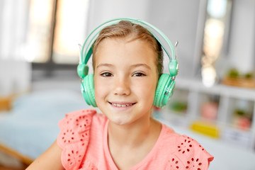 children and technology concept - portrait of smiling girl in headphones listening to music at home