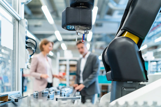 Robot in a modern factory hall with businessman and businesswoman in background