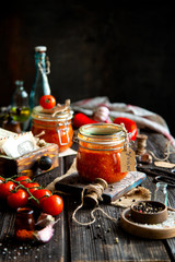 Homemade canned hot tomato sauce adjika in two glass jars standing on wooden board
