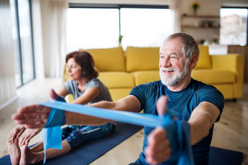 A senior couple indoors at home, doing exercise on the floor.