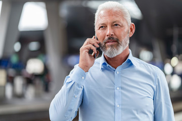 Mature businessman talking on cell phone at the station platform