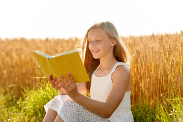 country, literature and leisure concept - smiling young girl in white dress reading book on cereal...