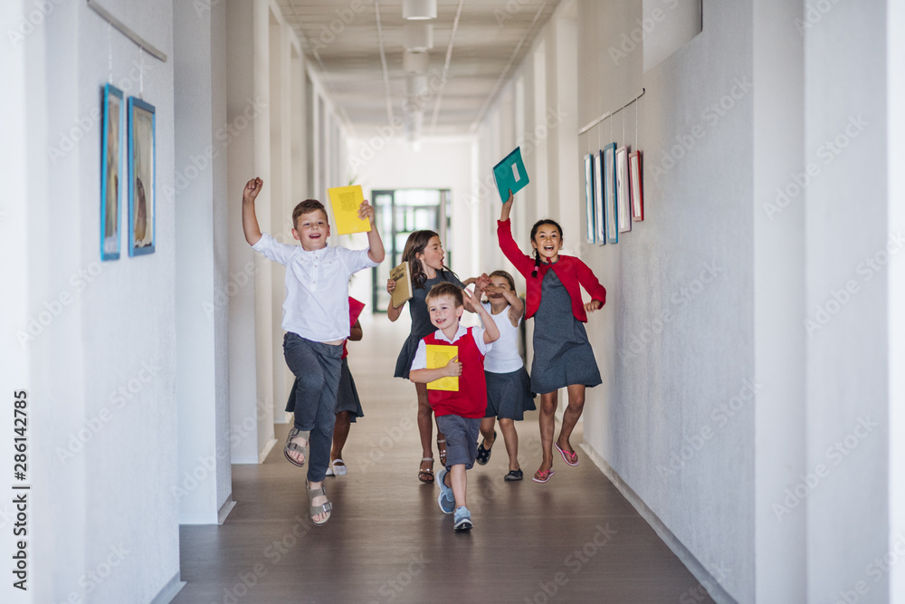 Wall mural A group of cheerful small school kids in corridor, running and jumping.