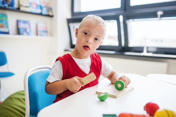 A down-syndrome school boy sitting at the desk in the classroom, learning.