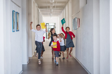A group of cheerful small school kids in corridor, running and jumping.