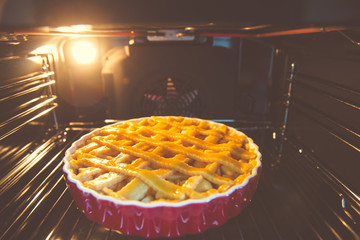 Fresh baked golden apple pie in red dish in oven at kitchen