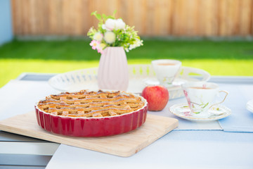Fresh baked apple pie, cup of tea and flowers on a table
