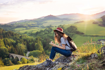 Young tourist woman traveller with backpack sitting in nature, writing notes.