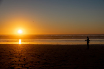 Silhouette of a man with a camera watching the sunset over the Atlantic Ocean from Agadir beach, Morocco, Africa