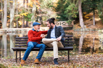 Senior father and his son sitting on bench by lake in nature, talking.