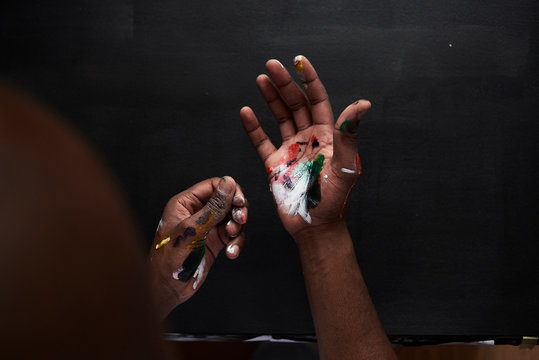 Dirty hands of artist with colorful paints against black background