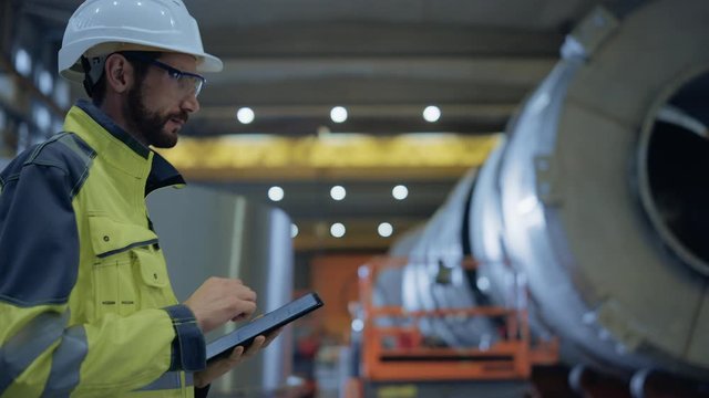 Heavy Industry Engineer Walk Through Pipe Manufacturing Factory, Use Digital Tablet Computer. Facility for Construction of Oil, Gas and Fuel Pipeline Transportation Products. Side View Slow Motion