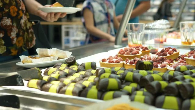 customer takes a pair of sweet pastries from a display case in a restaurant serving food
