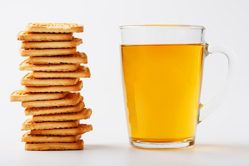A stack of golden wheat cookies and a mug of fragrant green tea in on a white background. Cookies laid out in a breakfast column and a golden highlight with tea mugs