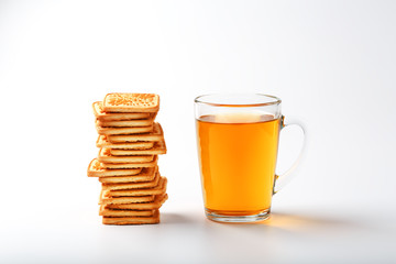 A stack of golden wheat cookies and a mug of fragrant green tea in on a white background. Cookies laid out in a breakfast column and a golden highlight with tea mugs