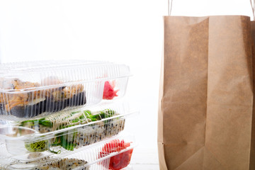 Stack of plastic boxes with sushi roll sets and paper bag. Food delivery