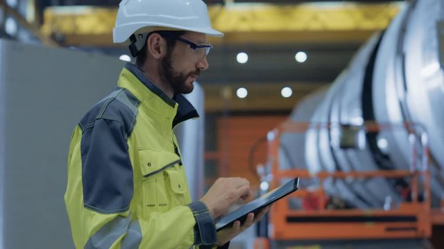 Heavy Industry Engineer Walk Through Pipe Manufacturing Factory, Use Digital Tablet Computer. Facility for Construction of Oil, Gas and Fuel Pipeline Transportation Products. Side View Slow Motion