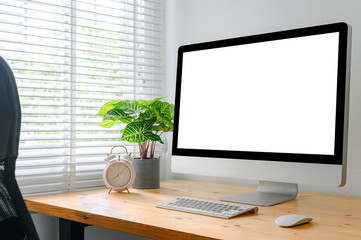 workspace with computer with blank white screen, and office supplies on a wooden desk