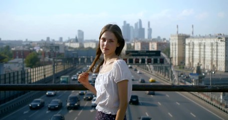 Young beautiful fashionable woman dressed in stylish clothes posing on the street bridge across the road