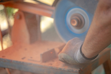 Construction worker cutting ceramic clay tiles elements for the lattice girder using the electric grinder machine on the construction site or warehouse