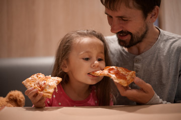 father feeding his cute daughter with pizza
