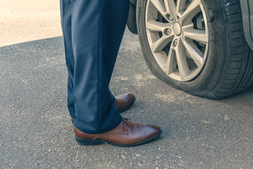 A businessman in a blue suit standing near his car and checks the degree of damage to a punctured...