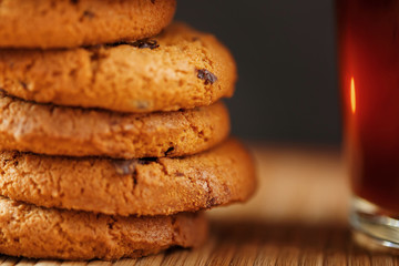 A pile of oatmeal cookies with chocolate chips and a mug of fragrant black hot tea in on a bamboo substrate, on a dark background. Handmade cookies for a healthy breakfast