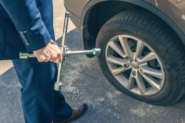 A businessman in a blue suit using cross wrench tighten the bolts wheel of punctured wheel. Hole in the tire. Concept