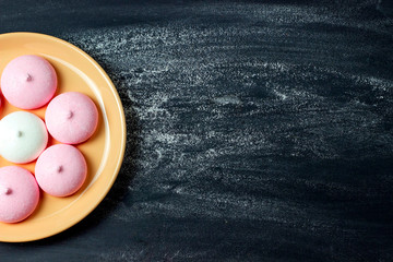 Meringue cookies in a pink plate on a black background. View from above.
