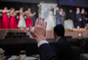 guests and members of the wedding party raise hands as they pray for the bride and groom.