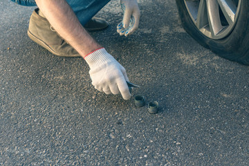 A man in the repair gloves trying to twist off the bolt for changing punctured wheel. Hole in the tire. Concept
