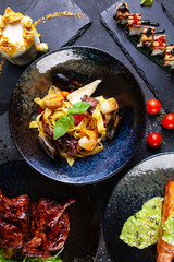 Top view on luxury restaurant food table with delicious meal. Flat lay food on dark background. Grilled meat, salmon, salads and suchi on table. Photo for menu, poster or banner